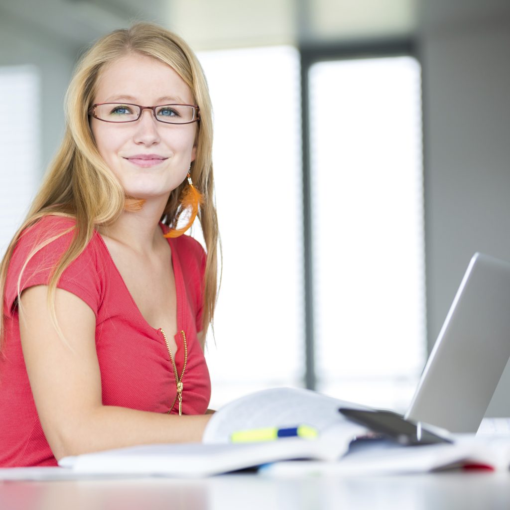 In the library - pretty, female student with books and laptop co Kvinne som jobber med e-læring